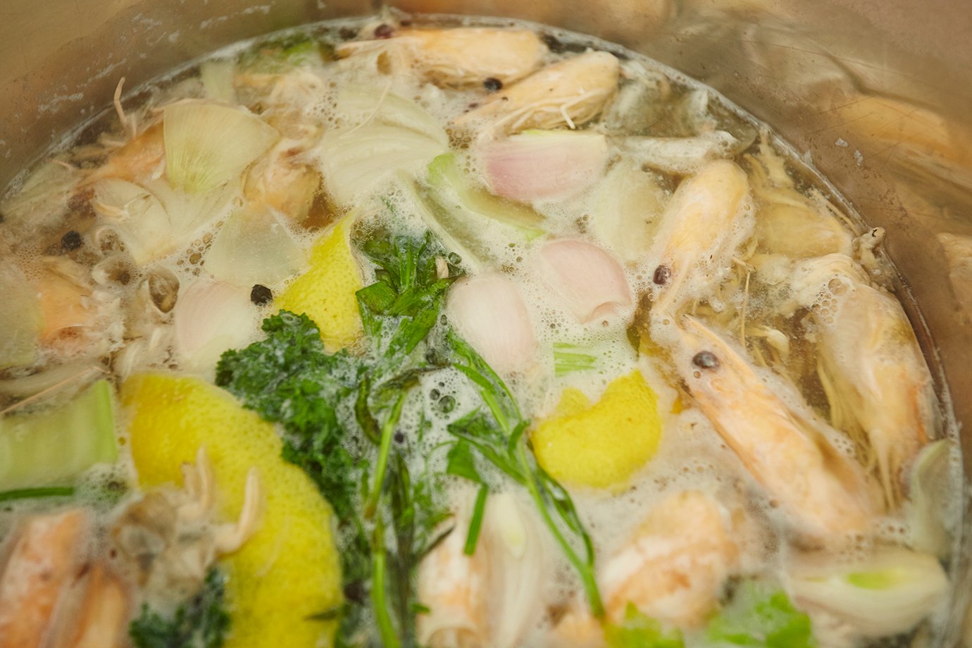 2. Garnelenköpfe und -schalen auf den Boden eines grossen Kochtopfs legen. Schalotten, Zwiebeln, Karotten und Sellerie sowie alle Kräuter hinzugeben. Die Zitrone waschen und spiralförmig schälen. Zitronenschale beifügen. Wein, Wasser und, falls verwendet, auch Noilly Prat dazu giessen. Die Pfefferkörner in den Sud geben, alles aufkochen, dann die Hitze reduzieren und den Sud auf kleinem Feuer 35 bis 40 Minuten sanft köcheln lassen. Den Sud durch ein feines Küchensieb passieren, darauf achten, dass die Zutaten mit der Kochkelle gut ausgepresst werden, um ein Maximum an Aroma zu erreichen.